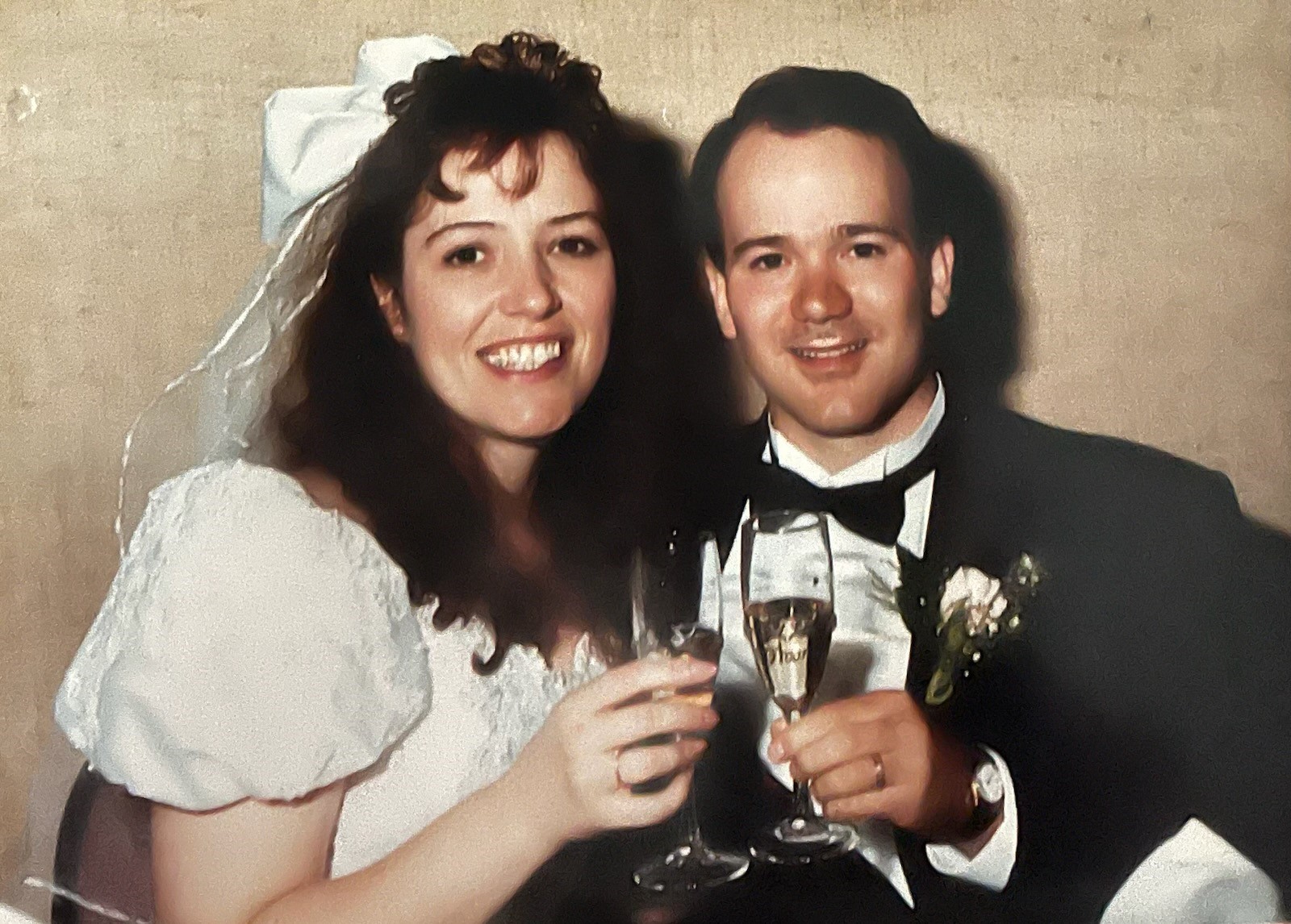 Tom and Lisa on their wedding day. They are toasting with glasses of champagne.