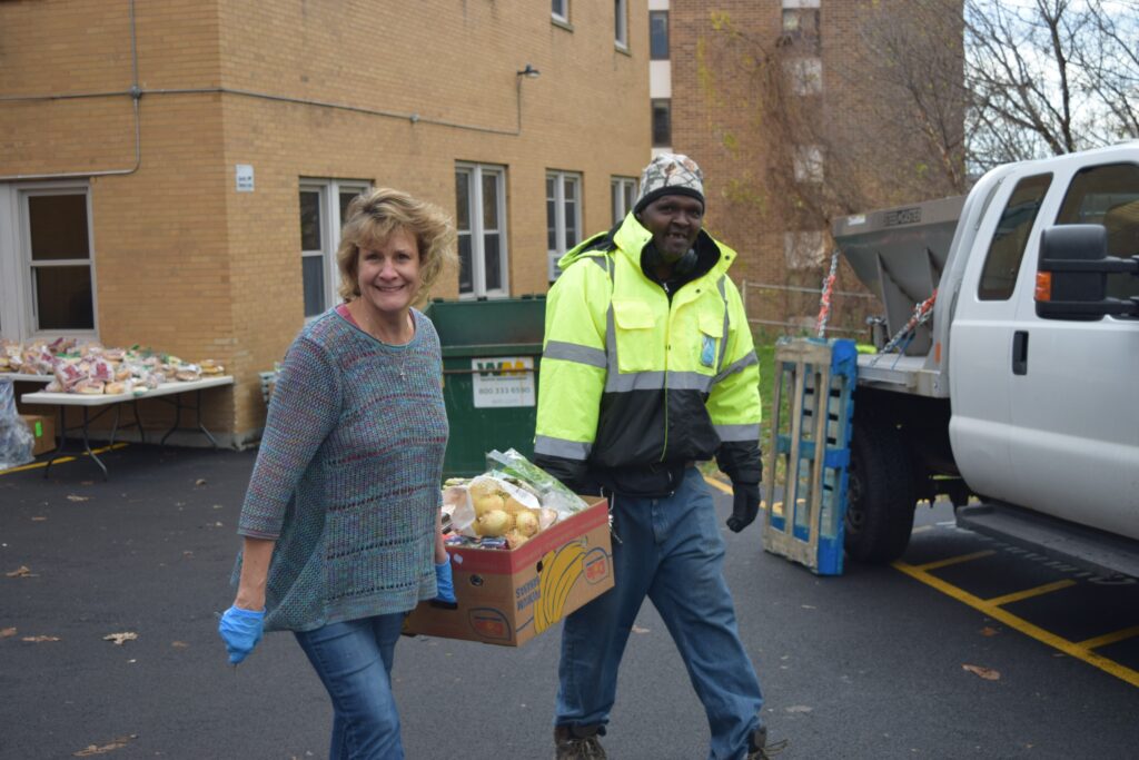 Two people carry a box full of food for CCOC's Fresh Food Distribution.