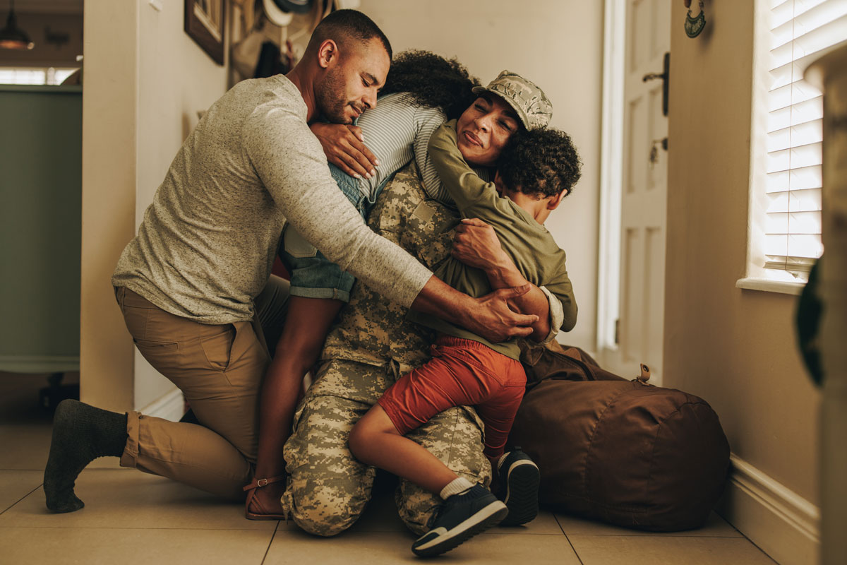 A family of four hugging by a front door. The mother is in military uniform and has just returned home.